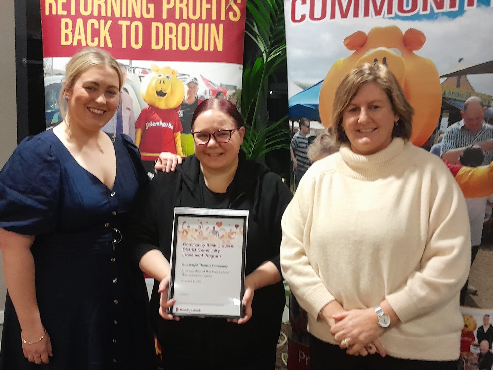 Ghostlight Theatre representatives Teigan Bliss and Renee Fallon accept funds from bank director Sonia Lombardo.