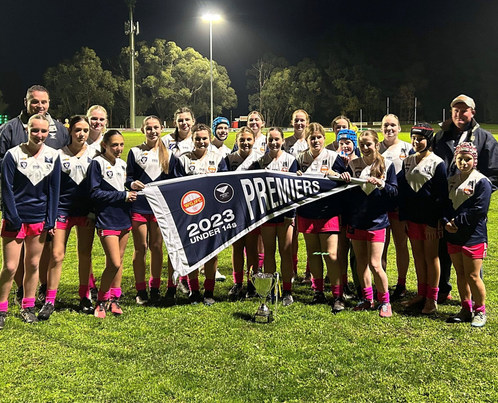 Unfurling the Warragul Blues under 14 girls flag are Stuart Dalton (vice president), Lucy Bates, Jaya Opteynde, Ankalie O'Regan, Natarlia Sweet, Alyssa Fitzgerald, Jae Tuckey, Skye Moles, Abbigail McDonald, Indi Olsson, Lily Huggins, Zaria Dalton, Pallas Jackman-Riches, Jasmine Terrill, Holly Pickles, Grace Patterson, Alisha Jamieson, Josie Malady, Jade Fitzgerald, Aster Moles and Dan Bates (2024 coach). Absent Paul Jameson (2023 coach).