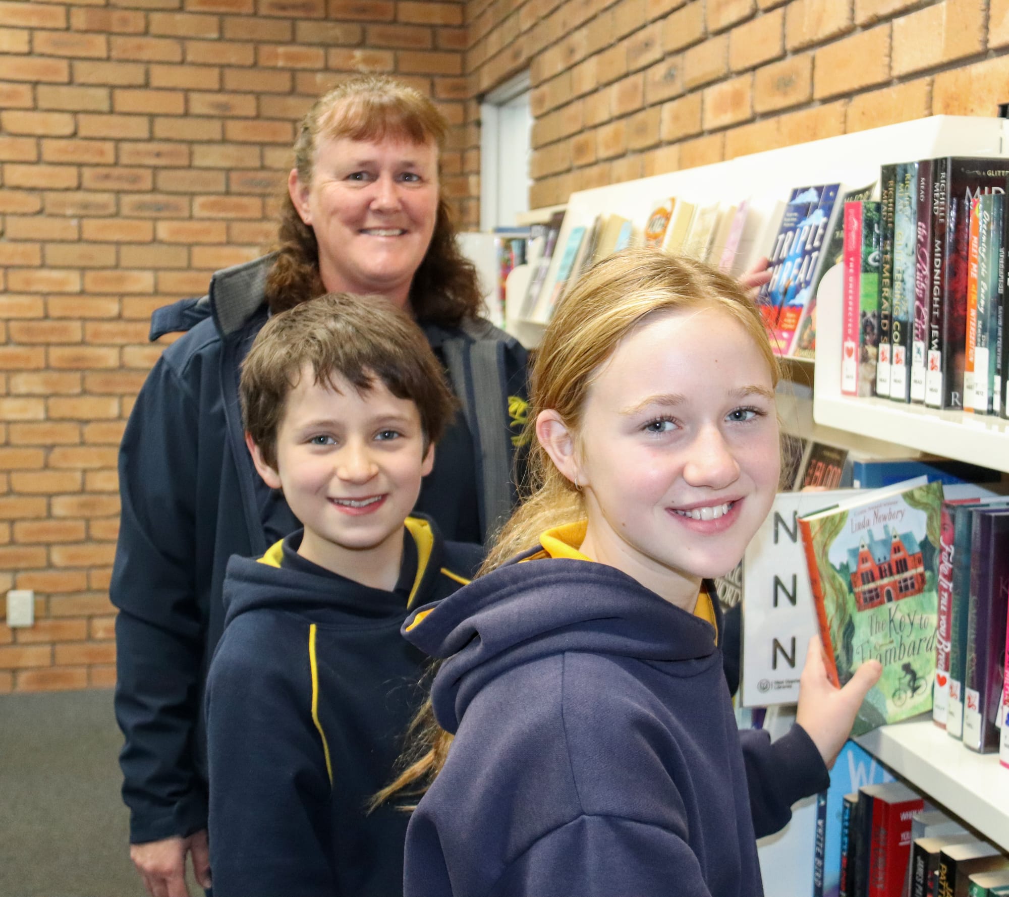 Principal Catherine Clerks (back) helps Angus Pollock and Erika Reynolds choose something to read.